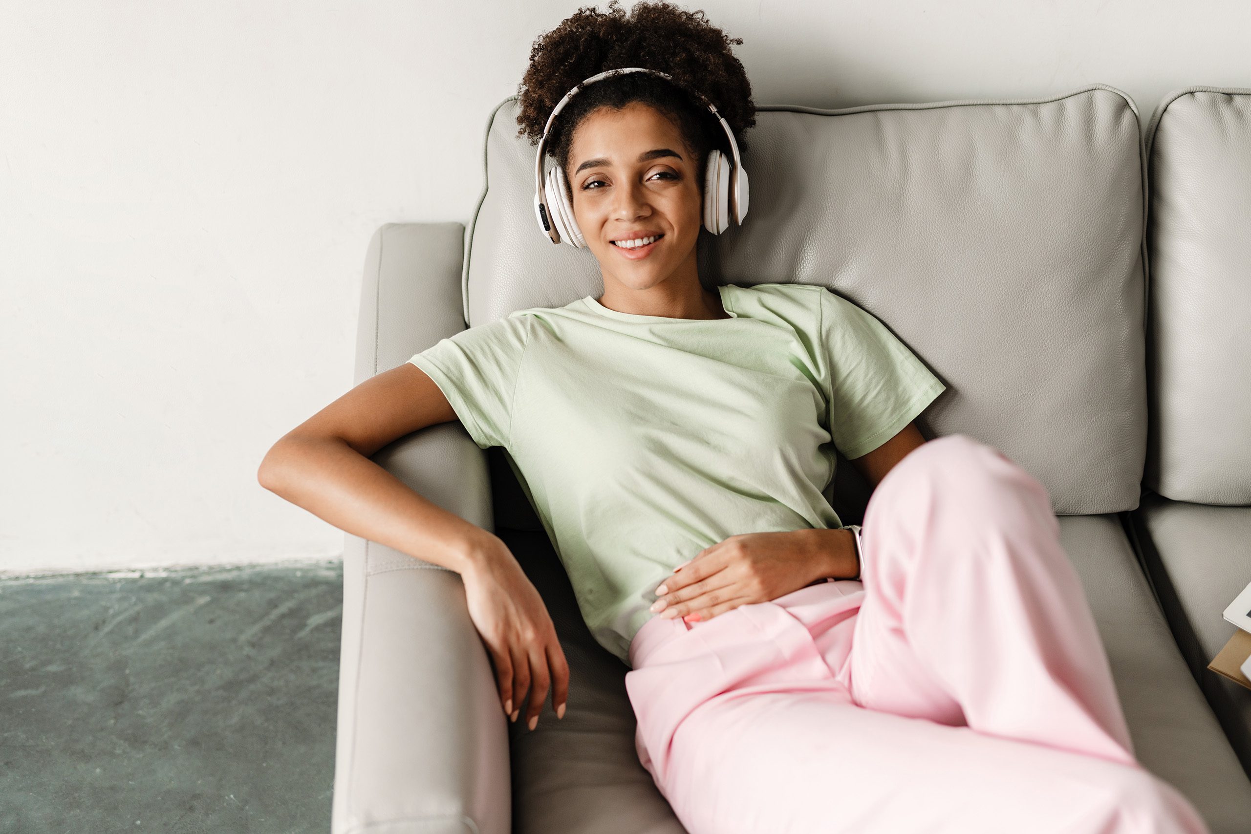 Young black woman listening music with headphones while sitting on couch